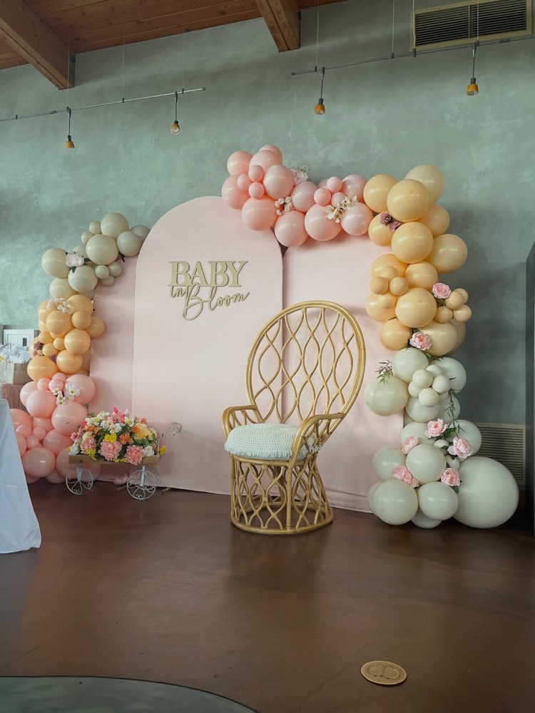 Baby in Bloom baby shower display with three panels, two balloon arches with florals and a wicker chair