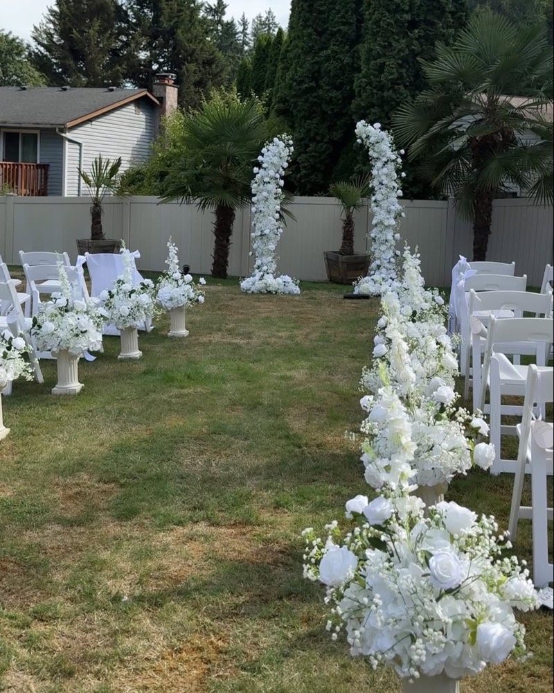 White floral arch at the end of a wedding aisle lined with floral arrangements
